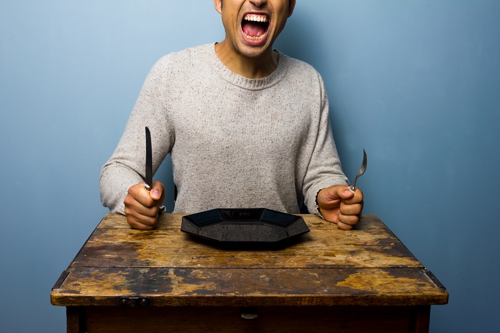 Hungry man sits at a table with plate, knife and fork Hungry man sits at a table with plate, knife and fork