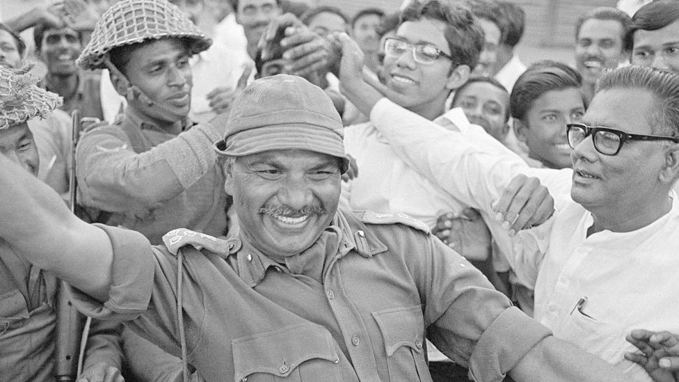 ब्रिगेडियर जनरल आर मिश्रा पूर्वी बंगालियों से घिरे हुए हैं. आर मिश्रा ढाका में भारतीय सेना का नेतृत्व कर रहे थे. 14 दिनों तक पाकिस्तान से चले युद्ध के बाद युद्धविराम पर सहमति बनी थी और बांग्लादेश का जन्म हुआ था. ब्रिगेडियर जनरल आर मिश्रा पूर्वी बंगालियों से घिरे हुए हैं. आर मिश्रा ढाका में भारतीय सेना का नेतृत्व कर रहे थे. 14 दिनों तक पाकिस्तान से चले युद्ध के बाद युद्धविराम पर सहमति बनी थी और बांग्लादेश का जन्म हुआ था.
